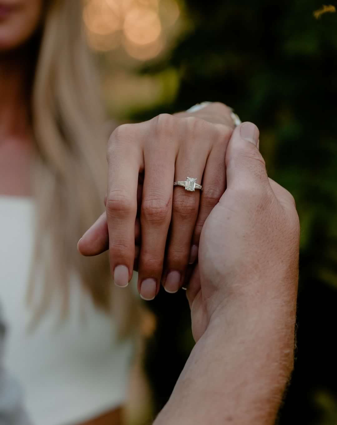 A couple holding hands, with an oval natural diamond solitaire engagement ring on her finger